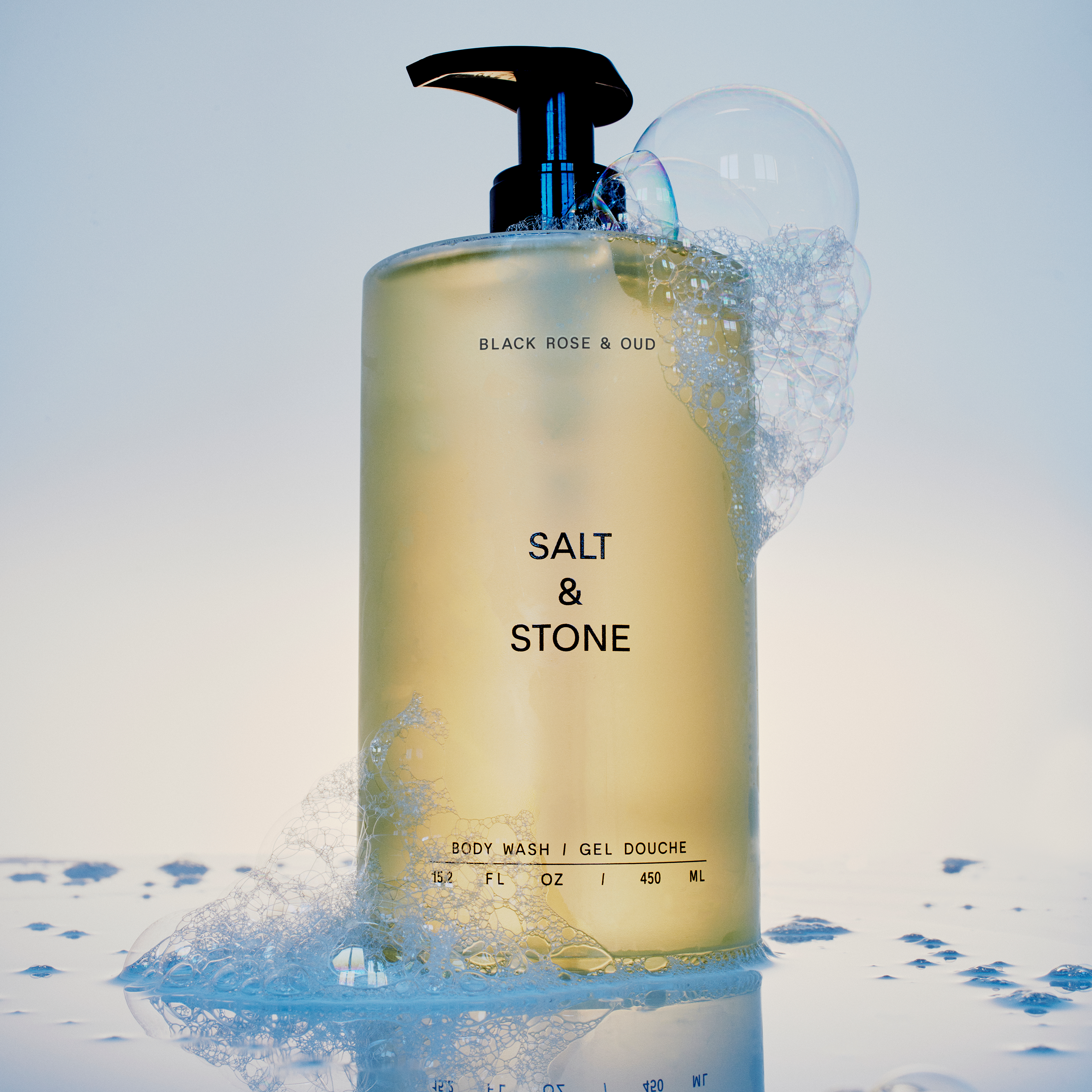 Bottle of Salt & Stone body wash with bubbles on a light blue background