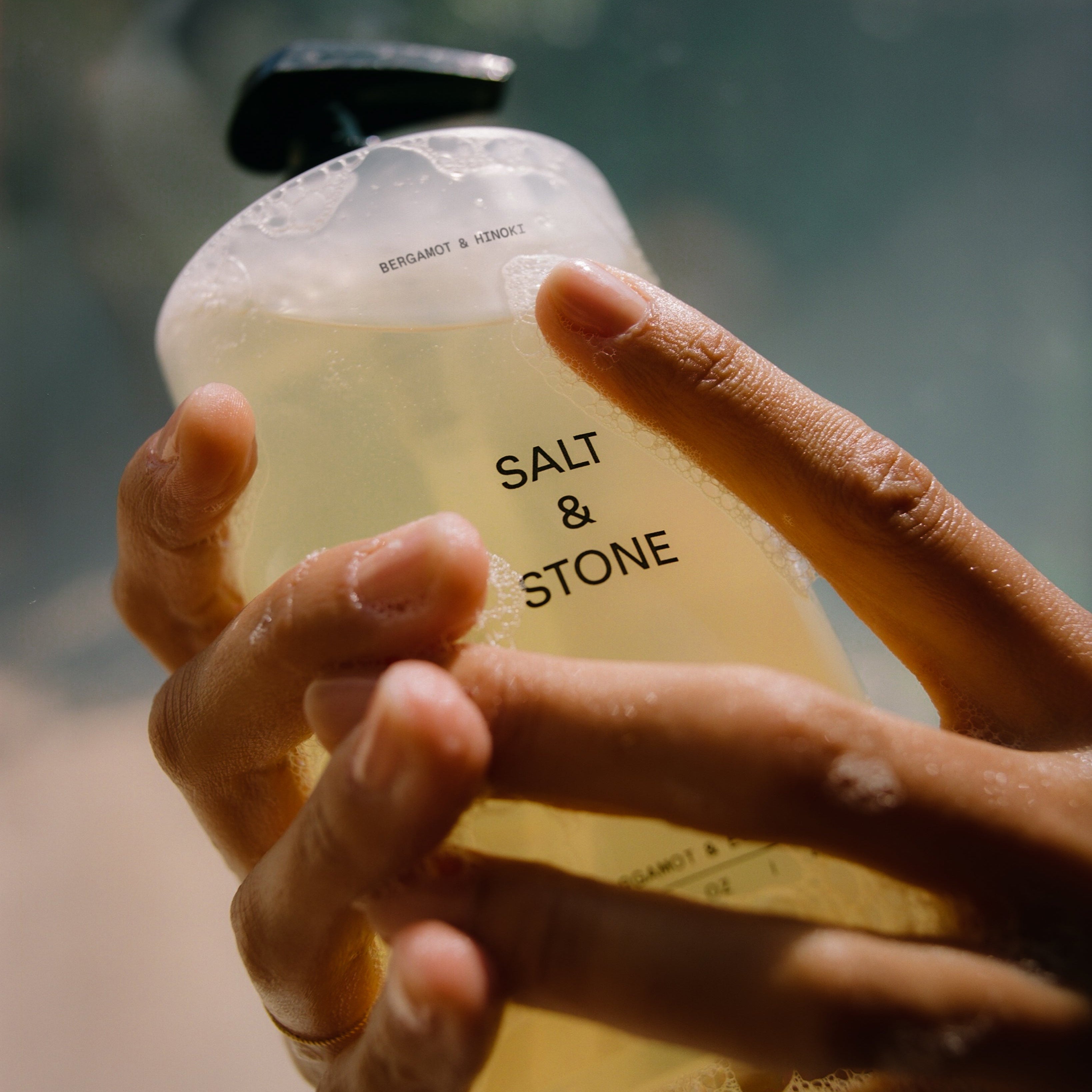 Hand holding a bottle labeled 'Salt & Stone' with a blurred background