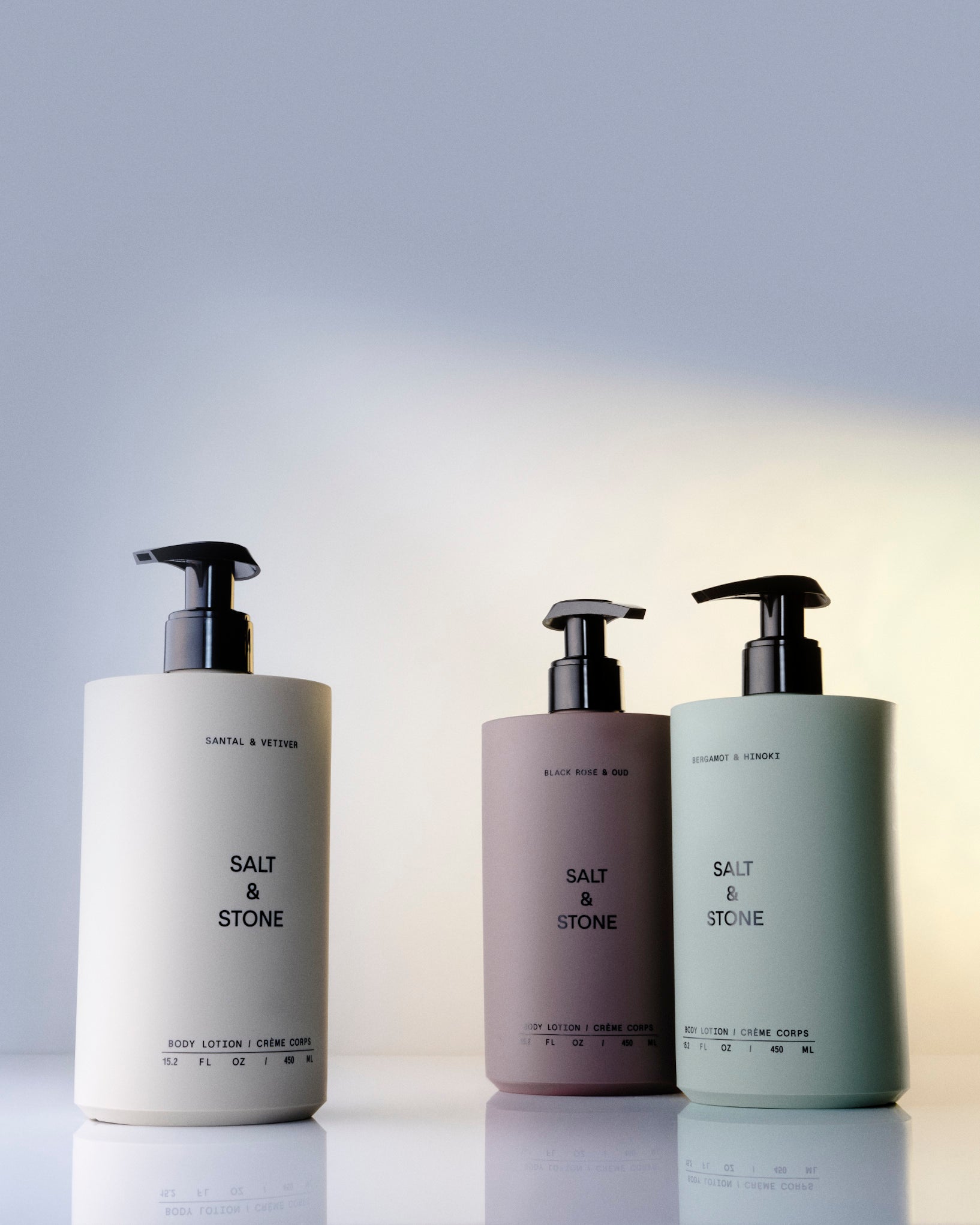 Three bottles of Salt & Stone products on a reflective surface with a gradient background.